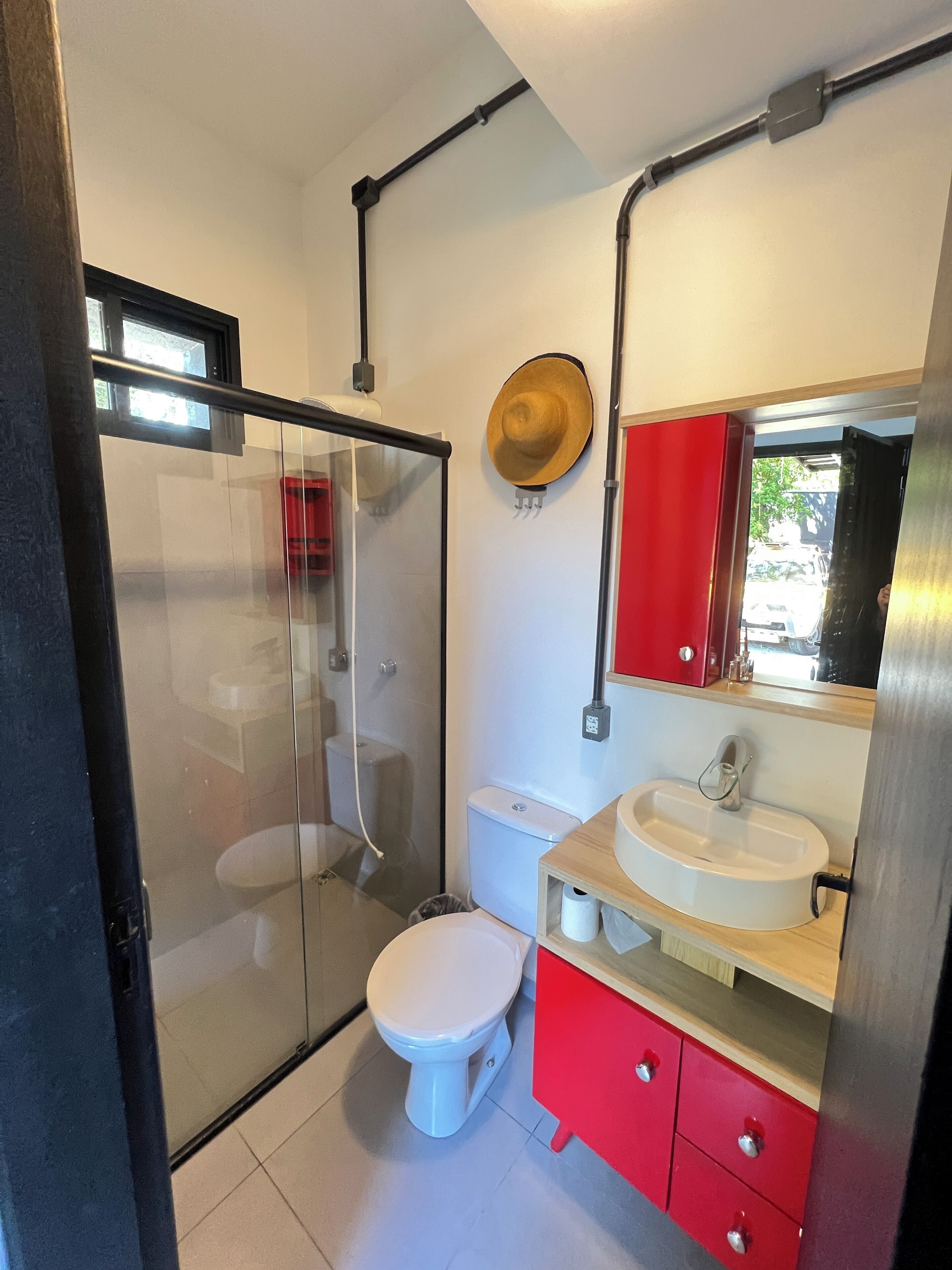 Un baño moderno con cabina de ducha de vidrio, inodoro blanco y tocador rojo con espejo.