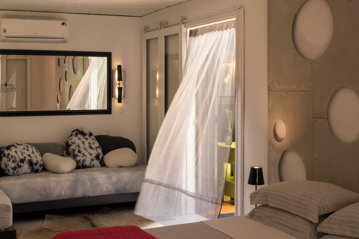 A modern bedroom with a large bed, a sofa, a mirror, and a window with curtains.
