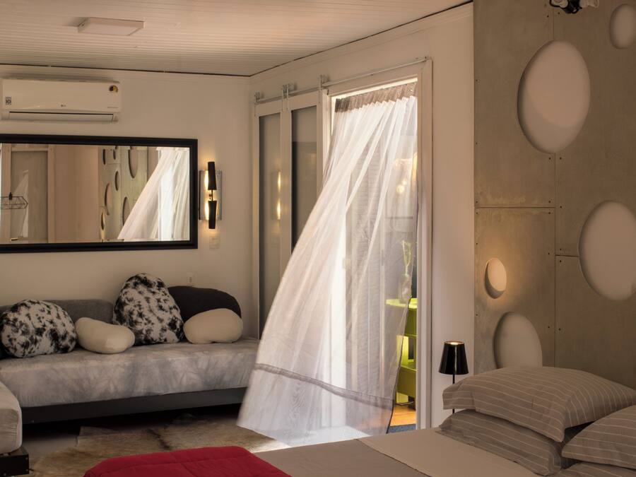 Een moderne slaapkamer met een groot bed, een bank, een spiegel en een raam met gordijnen.