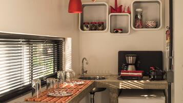 A compact kitchen with a countertop, a sink, a refrigerator, and red pendant lights.