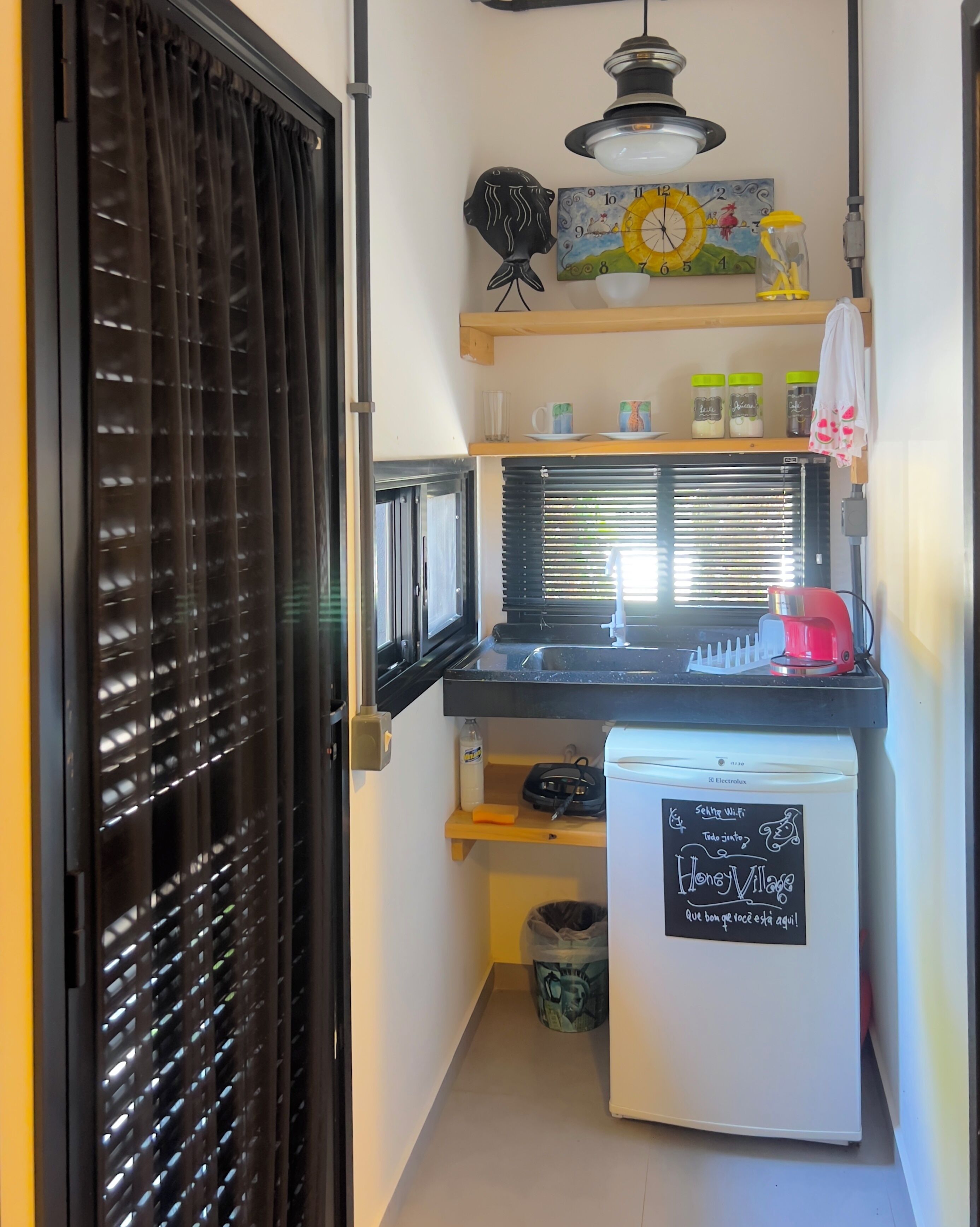 A compact kitchen with a refrigerator, a sink, and a window with blinds.