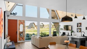 Un interior moderno con comedor, cocina y amplios ventanales que ofrecen vistas al exterior.