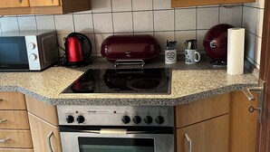 A kitchen with wooden cabinets, a microwave, a red kettle, a coffee maker, and a paper towel holder. - Apartment 1880 (Werne)