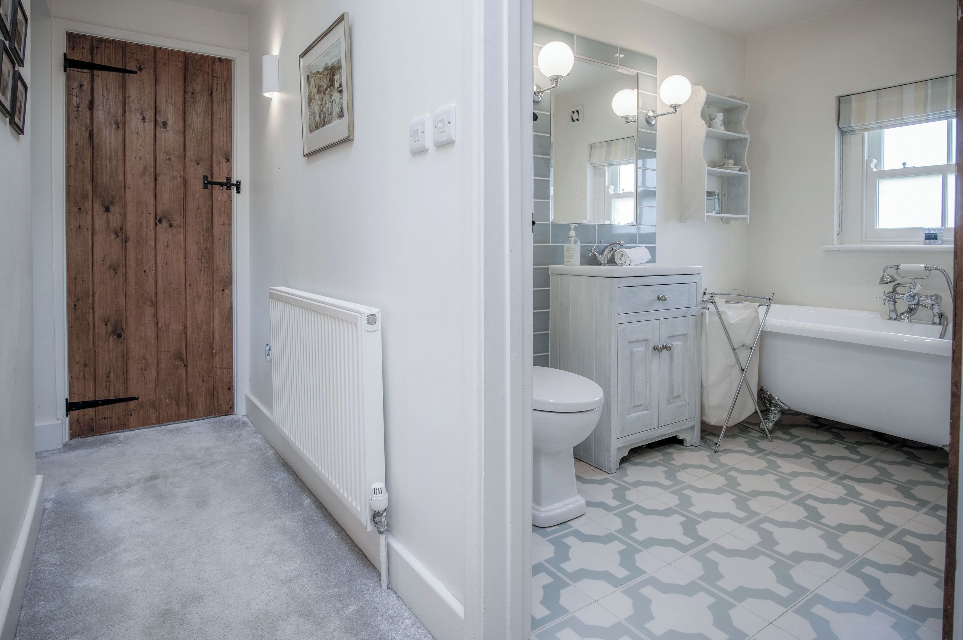 A bathroom with a white toilet, a white sink, and a white bathtub. There is a wooden door and a radiator on the wall.