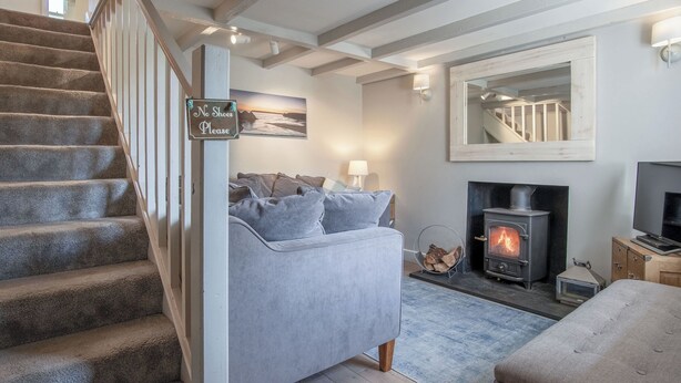 A staircase leading to a living room with a sofa, a fireplace, and a sign that reads "No Shoes Please". - Dollars Cottage - 4 Bed - Llangennith (Swansea)