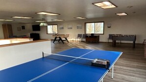 Una habitación con mesa de ping pong, mesa de fútbol y un escritorio con computadora.