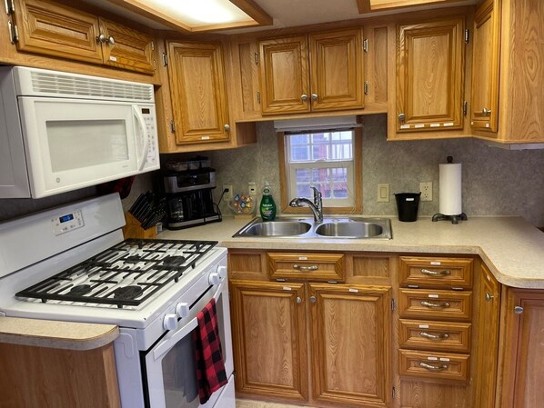 A kitchen with wooden cabinets, a white stove, a microwave, a sink, and a window.