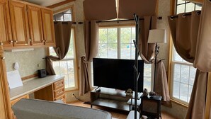 Un interior de caravana acogedor con televisor de pantalla plana, armarios de madera y ventanas amplias.