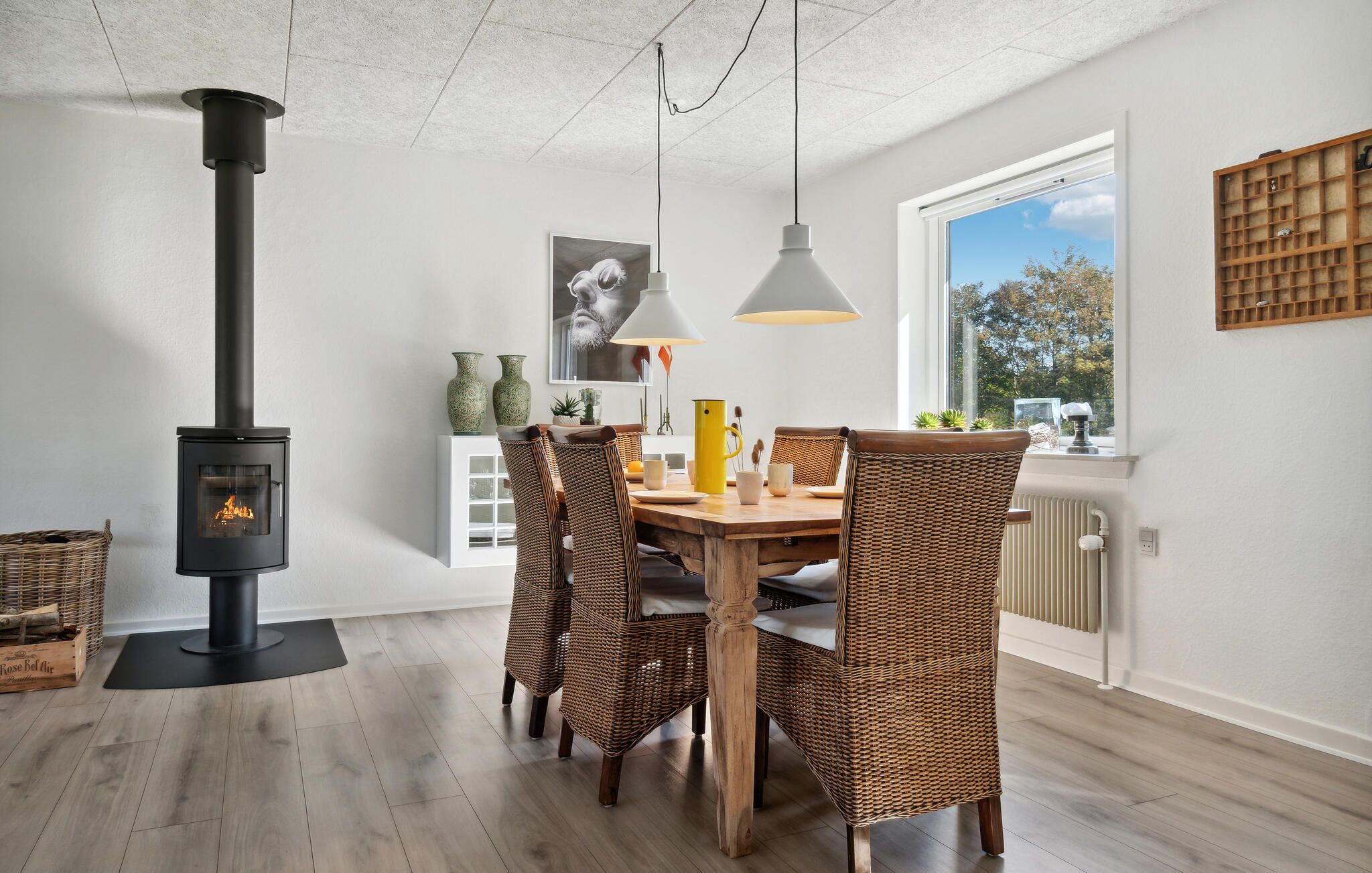 Un comedor moderno con estufa de leña, sillas de mimbre y un amplio ventanal con vistas al exterior.