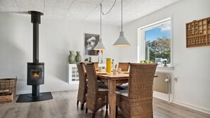 A modern dining area with a wood-burning stove, wicker chairs, and a large window providing a view of the outdoors. - Awesome home in Nykøbing M (Nykøbing M)