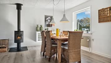 Un comedor moderno con estufa de leña, sillas de mimbre y un amplio ventanal con vistas al exterior.