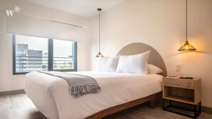 A bedroom with a large bed, a nightstand, a window with a view of buildings, and two pendant lights. - Wynwood The Classic in San Isidro (Lima)