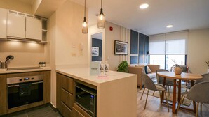 A modern kitchen with built-in appliances, a central island with seating, and a dining area with a round table and chairs. - Wynwood The Classic in San Isidro (Lima)