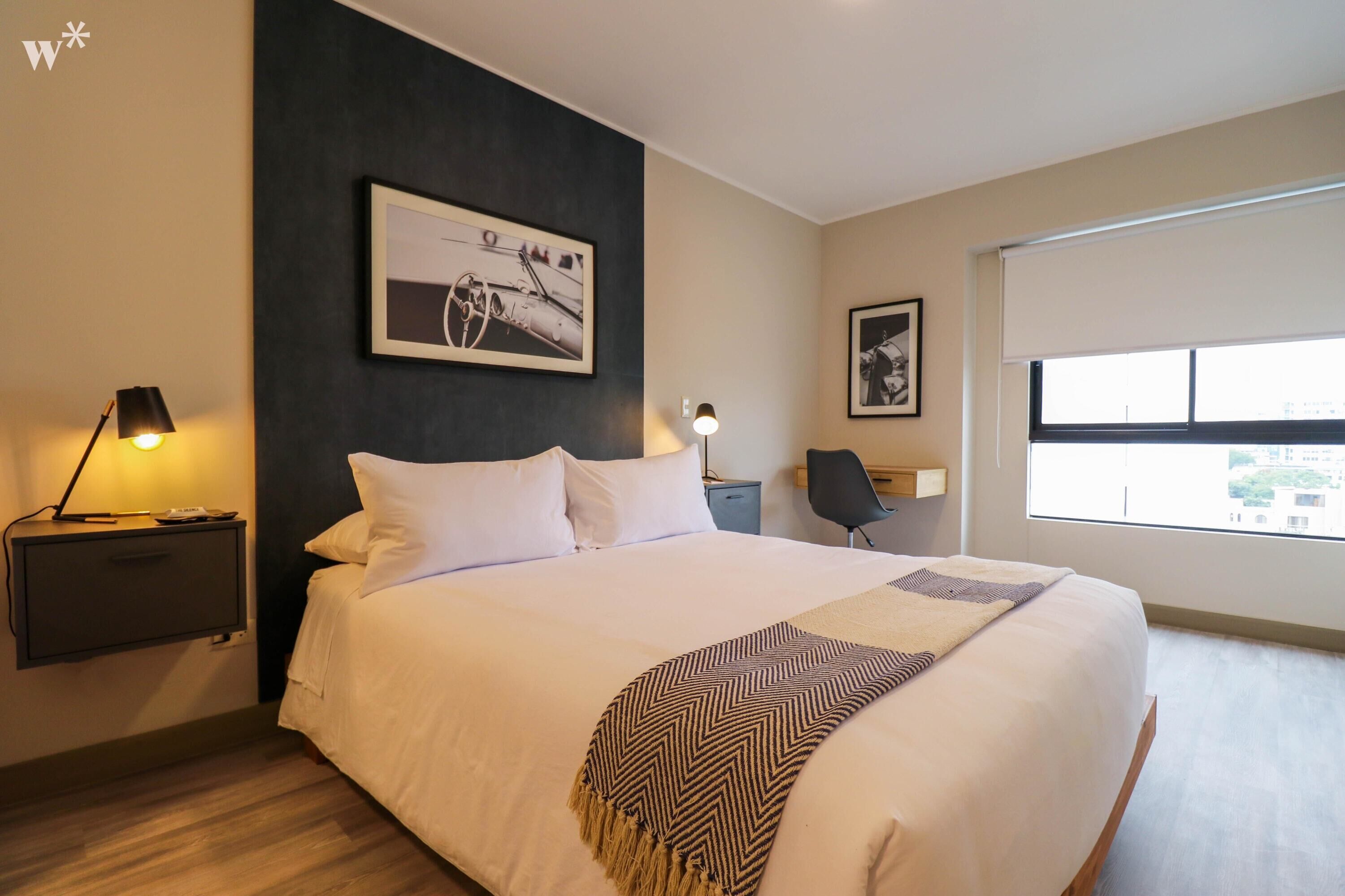 Ein modernes Hotelzimmer mit einem großen Bett, zwei Nachttischen mit Lampen, einem Schreibtisch und einem Stuhl.