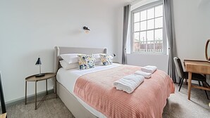 A neatly arranged bedroom with a bed, bedside table, lamp, and a desk with a chair. - County House Escape - courtyard & free parking (York)
