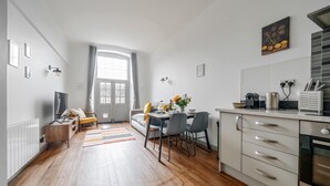 A modern kitchen with white cabinets, a dining area with a table and chairs, and a sofa in the background. - County House Escape - courtyard & free parking (York)