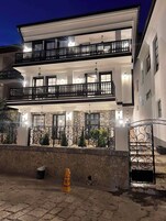 Un edificio de varios pisos con balcones, paredes de piedra y un área pavimentada.