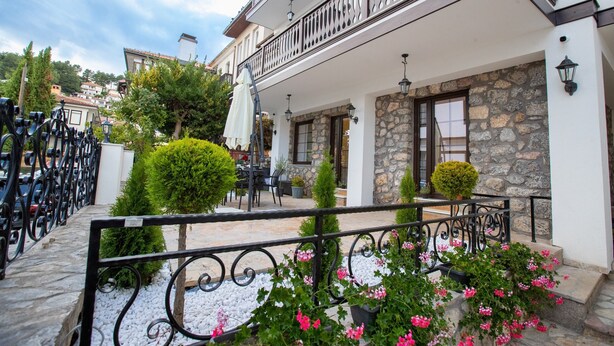 A building with a stone facade, a balcony with a wrought iron railing, and a small patio area with potted plants and outdoor seating. - Villa Pupin SARAISTE (Ohrid)