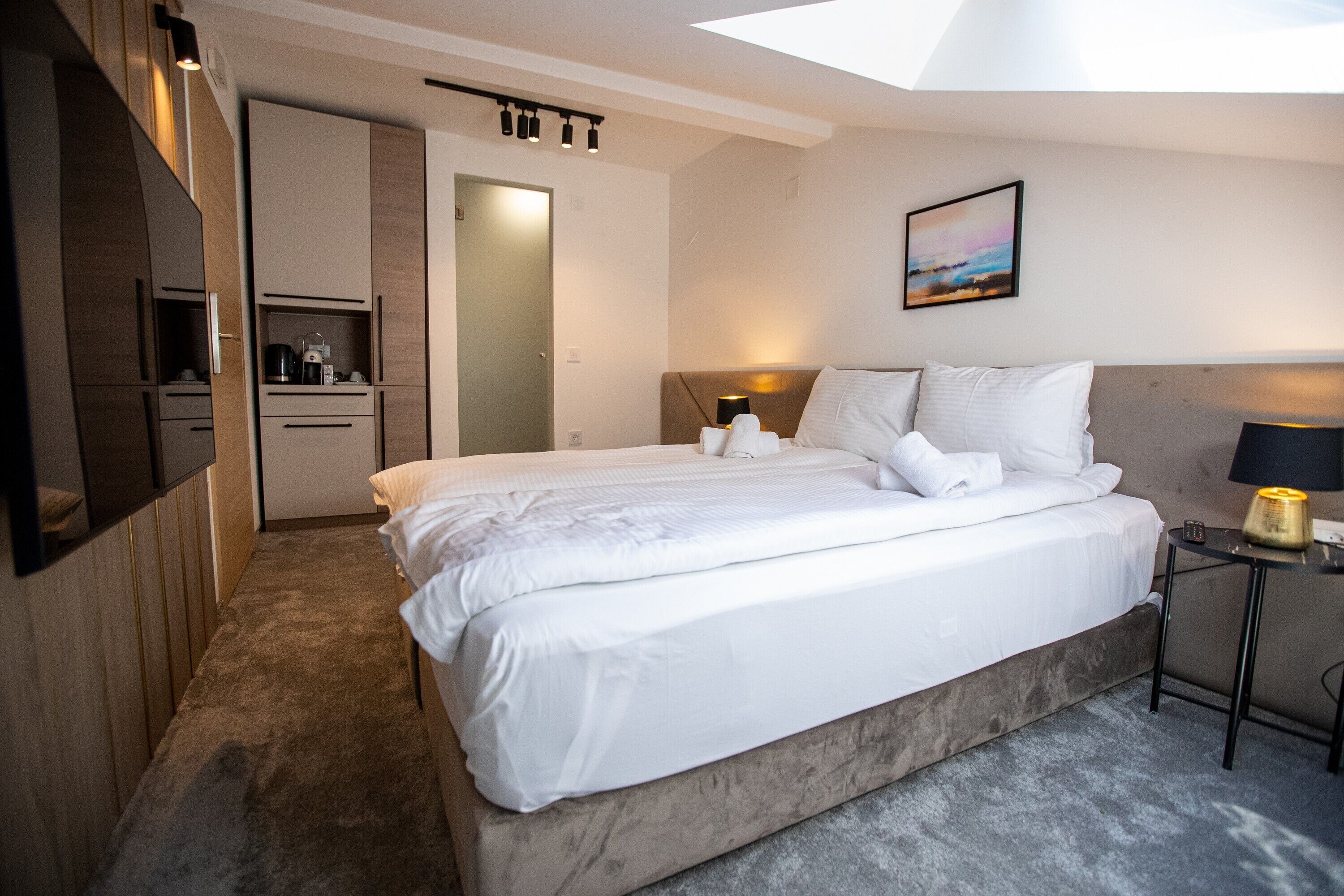 Ein modernes Hotelzimmer mit einem großen Bett, einem Nachttisch, einem Schreibtisch und Blick zum Himmel durch ein Oberlicht.