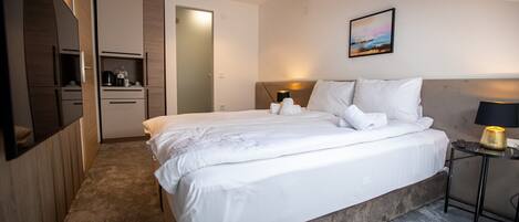 A modern hotel room with a large bed, a bedside table, a desk, and a view of the sky through a skylight.