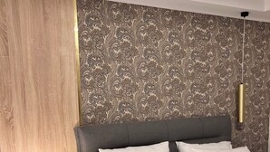A bedroom with a bed, a nightstand with a lamp, and a patterned wallpaper. - Villa Pupin SARAISTE (Ohrid)