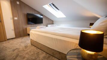 Une chambre moderne avec un grand lit, un téléviseur à écran plat fixé au mur, une lucarne et une table de chevet avec une lampe.