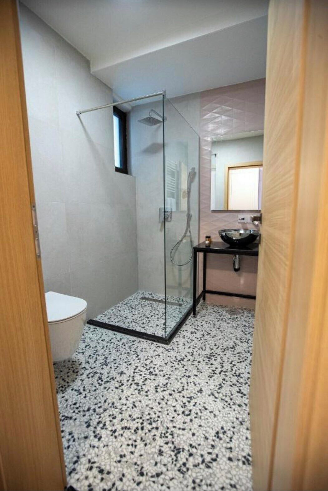 A modern bathroom with a glass-enclosed shower, a toilet, and a sink with a mirror above it.
