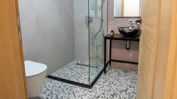 A modern bathroom with a glass-enclosed shower, a toilet, and a sink with a mirror above it.