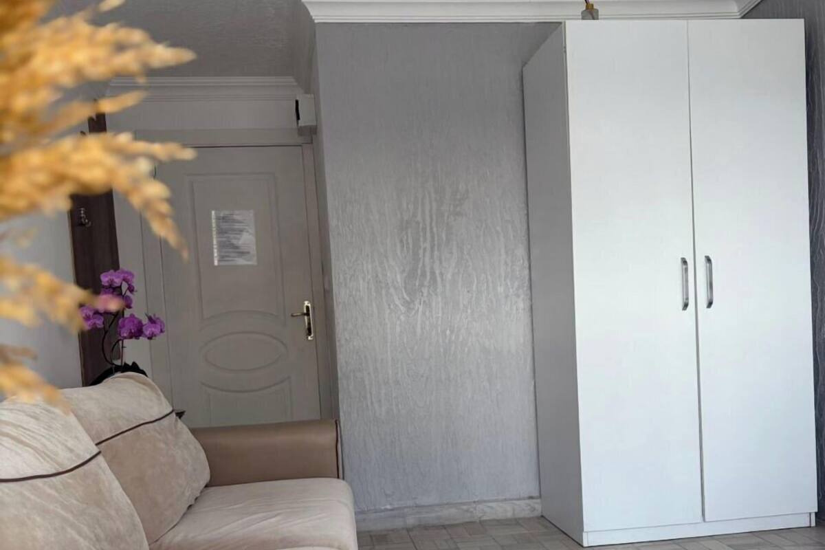 Une pièce avec un canapé beige, une armoire blanche et un sol carrelé.