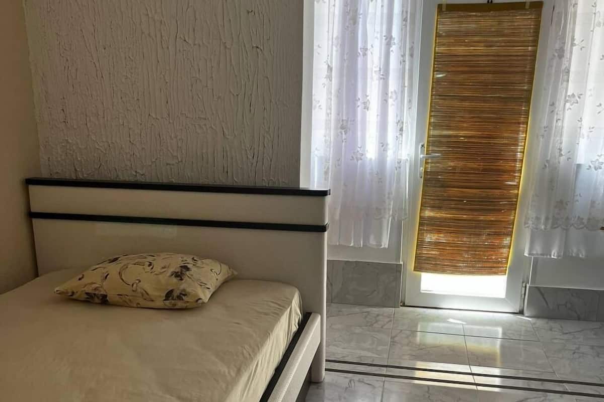 Une chambre à coucher avec un lit, une tête de lit, une fenêtre avec des rideaux et une vue sur l’extérieur.