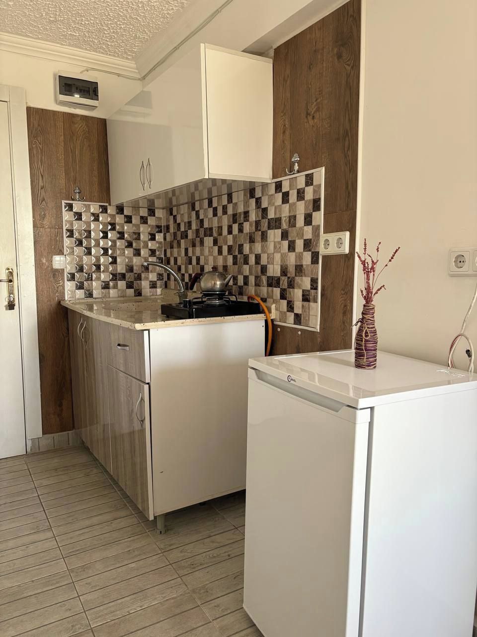 A compact kitchen with a checkered backsplash, a built-in oven, and a small refrigerator.