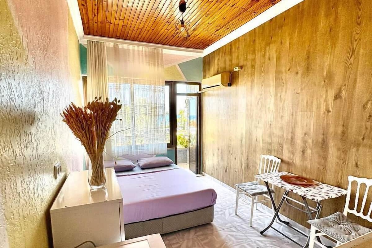 Une chambre moderne avec un plafond en bois, un lit, une petite table avec des chaises et une vue à travers une porte vitrée.