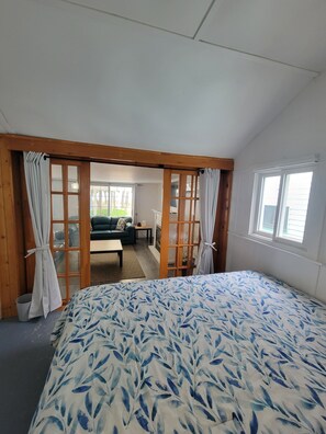 Une chambre avec un grand lit, un plancher en bois et une vue sur un espace de vie comprenant un canapé et une table.