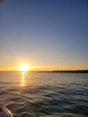Un coucher de soleil sur une étendue d’eau calme, avec une côte visible au loin.