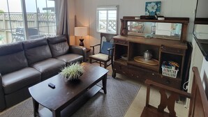 Een woonkamer met een bruine leren bank, een houten salontafel, een houten dressoir en een groot raam.