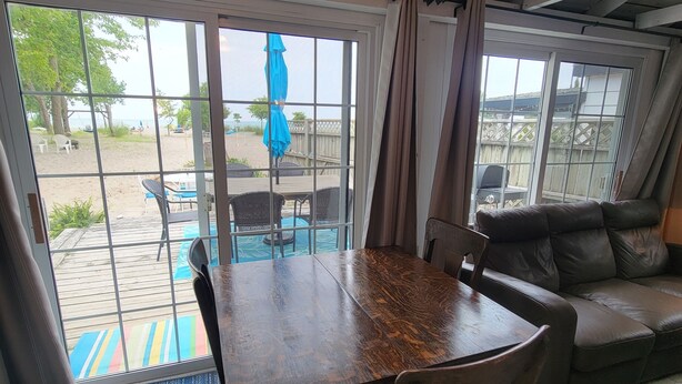 Een kamer met een houten eettafel, stoelen, een bank en uitzicht op het strand door grote glazen schuifdeuren.