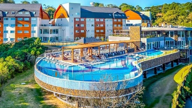 A modern hotel with a circular pool, multiple buildings, and lush greenery. - Golden Gramado Laghetto Resort - MC (Gramado)