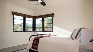Ein Schlafzimmer mit einem Bett, einem Deckenventilator und zwei Fenstern mit Jalousien.