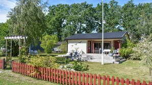A small, single-story house with a porch, surrounded by a red picket fence.