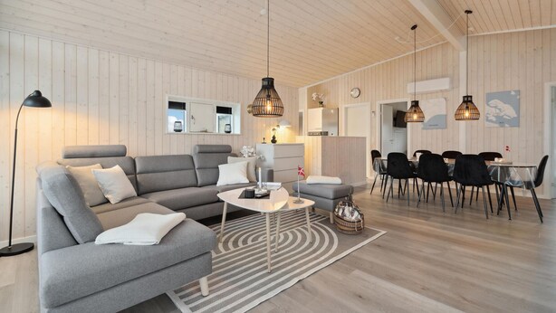 Una sala de estar moderna con un sofá gris, una mesa de centro y una zona de comedor con sillas negras y una mesa.