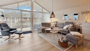 Una sala moderna con sofá, sillón y mesa de centro, un balcón con barandillas blancas y techo de madera.