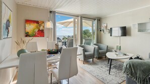 A modern living room with a dining area, a large window with a view, and a flat-screen TV mounted on the wall. - Pet friendly apartment in Allinge (Allinge)