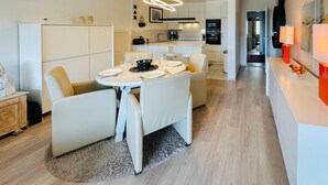 Una cocina moderna con muebles blancos, un comedor con mesa y sillas redondas, y una sala de estar con sofá y mesa de centro.