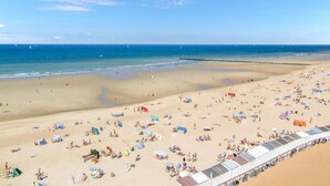 Una playa extensa con numerosas tumbonas y sombrillas, cielo despejado y mar tranquilo.