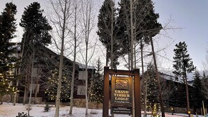 Schild für Grand Timber Lodge, mit Steinunterbau und Holzrahmen, umgeben von Bäumen und Schnee.