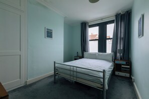 A bedroom with a metal bed frame, a bedside table, a lamp, and a window with curtains.
