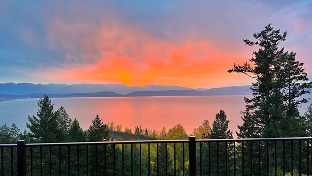 A scenic view of a lake with mountains in the background, a railing in the foreground, and trees around.