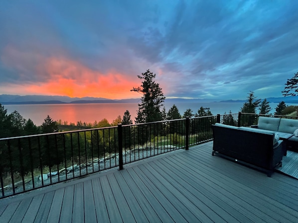 Um terraço com vista para um lago e montanhas ao pôr do sol.