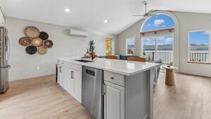A spacious kitchen with a large island, white cabinetry, and a view of the outdoors through large windows.
