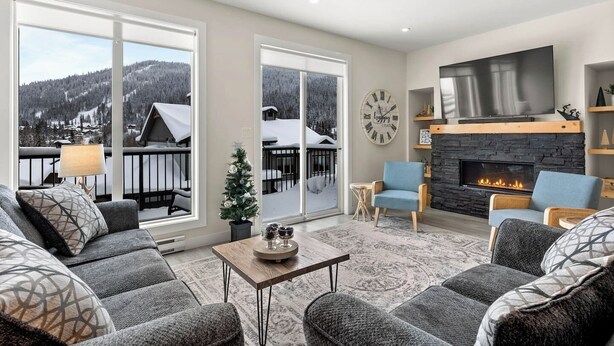 A spacious living room with a fireplace, comfortable seating, and a view of a snowy mountain landscape through large windows. - Spacious Alpine Retreat - w/Hot Tub (Sun Peaks)